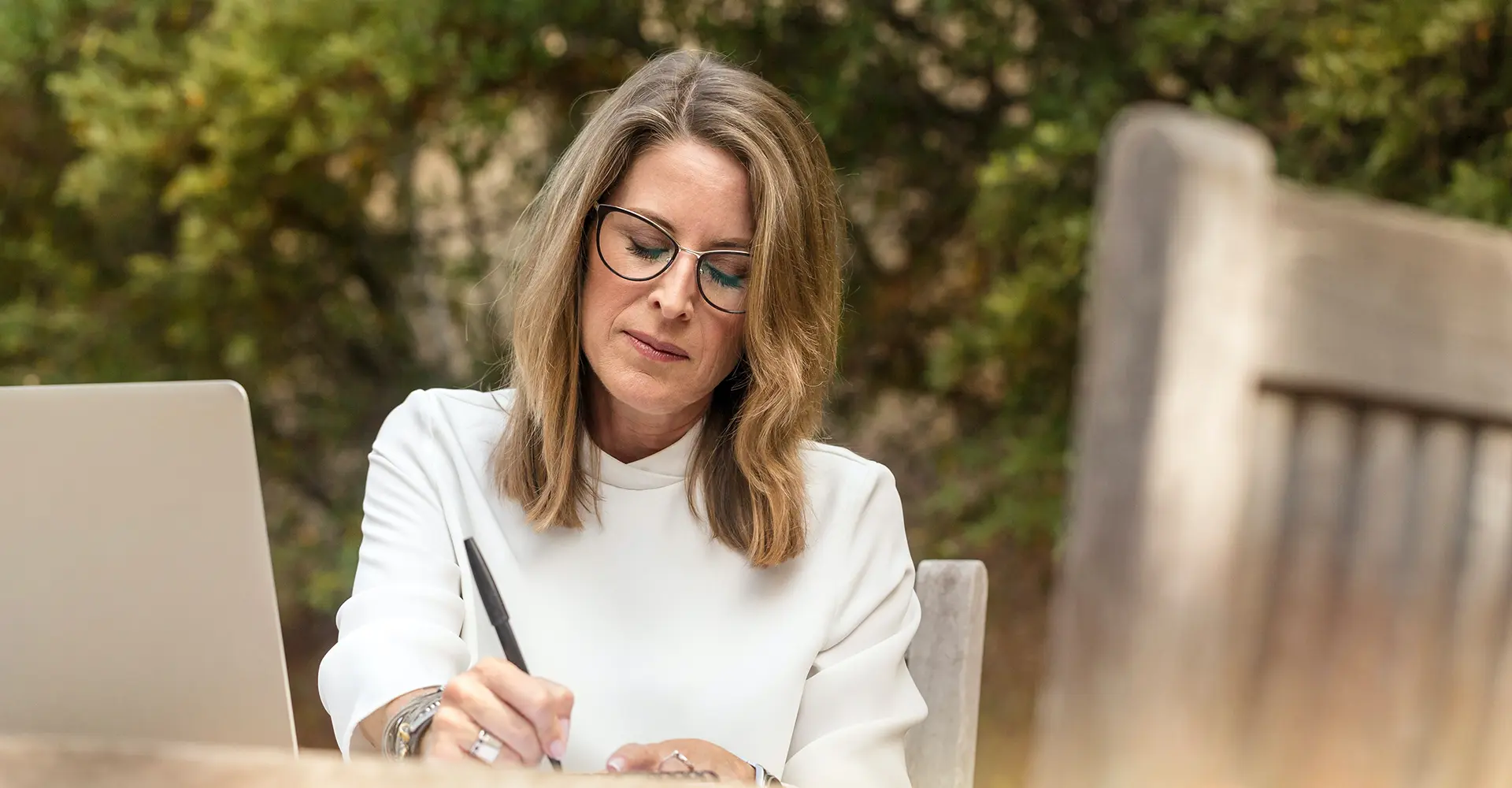 blonde-caucasian-woman-in-glasses-writing-note-card-to-friend-sitting-outside